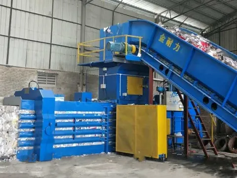 A horizontal baling press with stacked bales of baled paper beside it